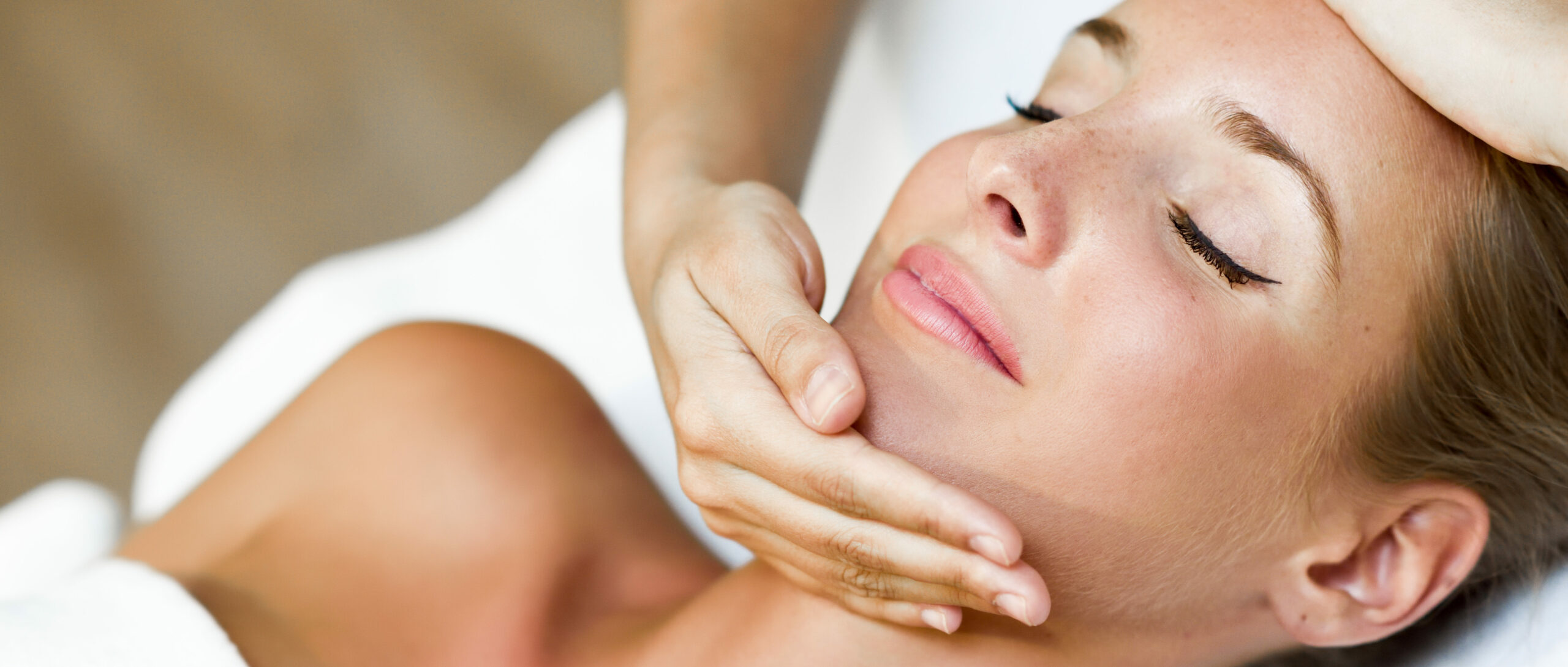 Mulher deitada, recebendo uma massagem no rosto