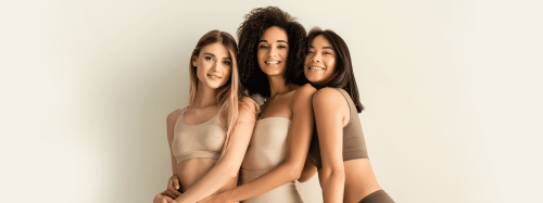 Três mulheres diversas sorrindo e se abraçando, mostrando a beleza natural e positividade corporal.